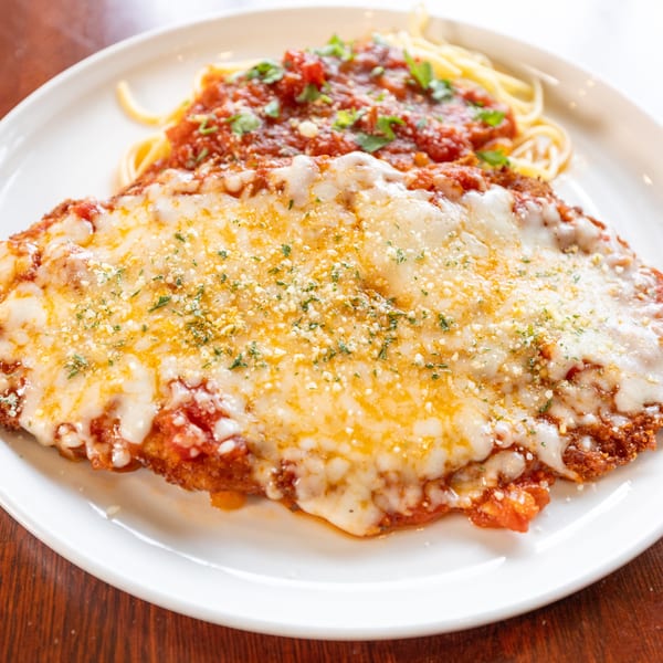 Chicken Parmesan with melted cheese and red sauce, served with spaghetti on a white plate.