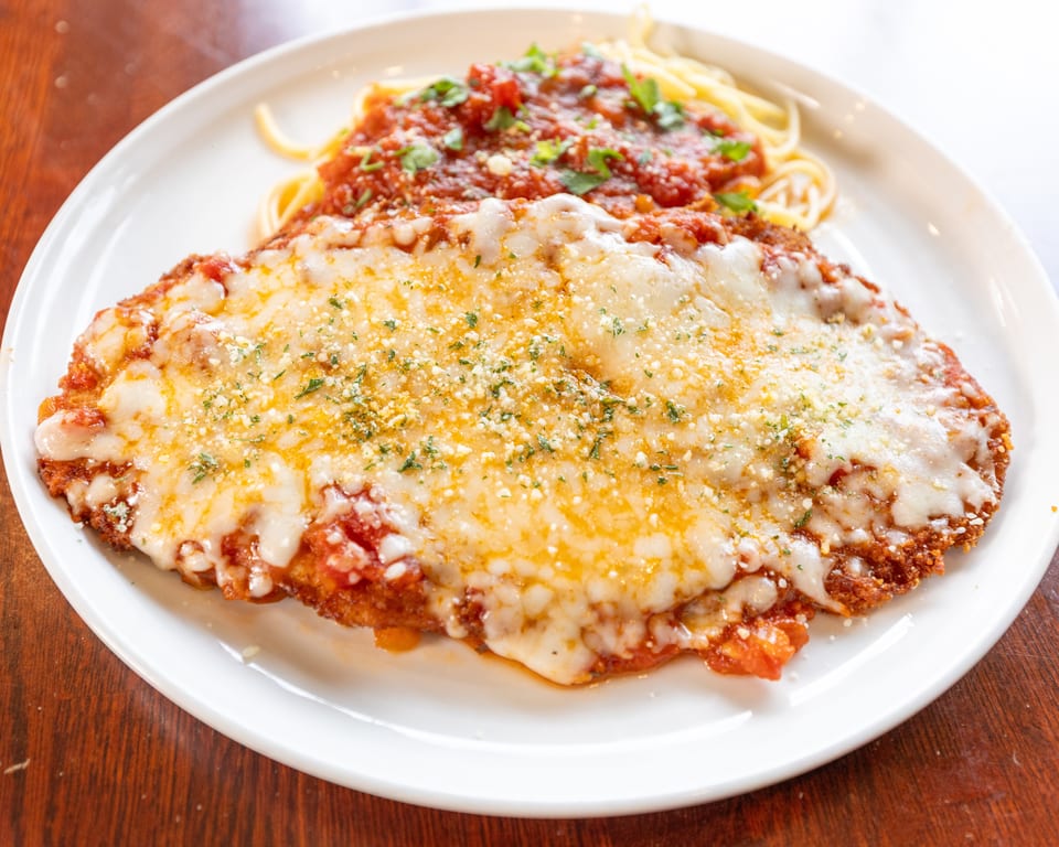 Chicken parmesan with melted cheese and red sauce, served with spaghetti on a white plate.