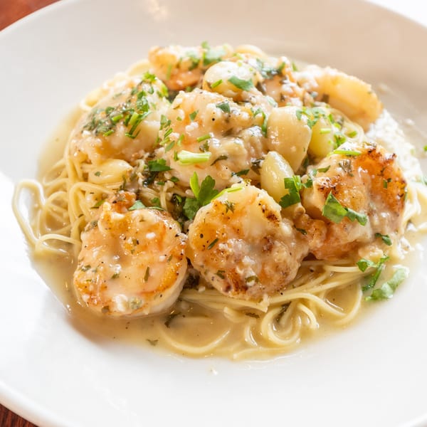 Shrimp scampi with spaghetti, garlic, and parsley in a creamy sauce on a white plate.