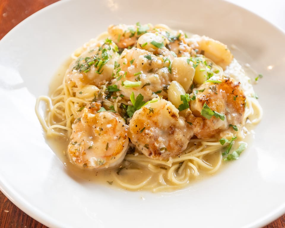 Shrimp scampi with spaghetti, garlic, and parsley in a creamy sauce on a white plate.