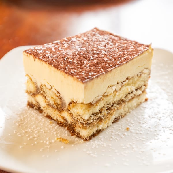 A slice of tiramisu with layers of cake and cream, dusted with cocoa and powdered sugar.