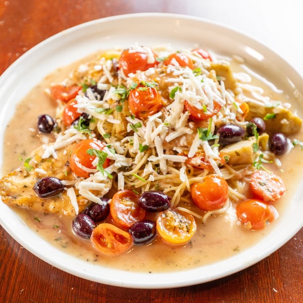 Chicken piccata with spaghetti, cherry tomatoes, olives, and shredded cheese in a creamy sauce.