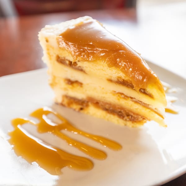 Slice of layered cake with dulce de leche filling and caramel drizzle on a white plate.