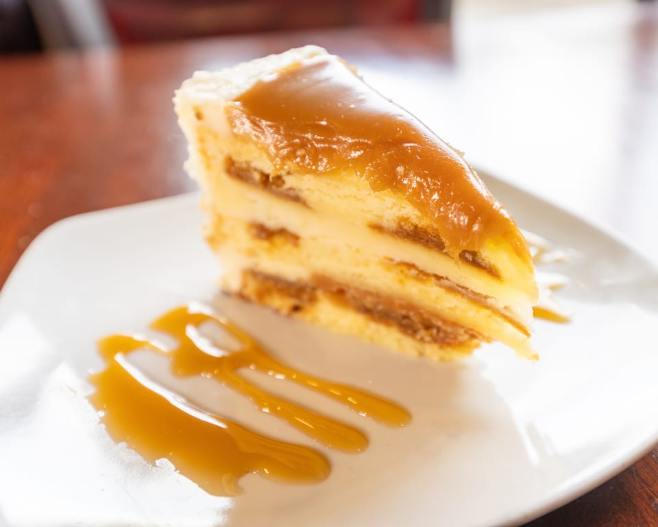 A slice of layered cake with dulce de leche filling and caramel drizzle on a white plate.