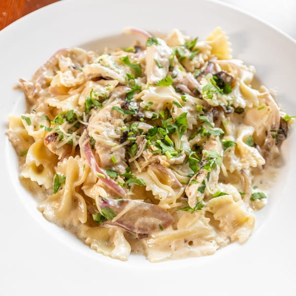 Creamy bowtie pasta with chicken, mushrooms, red onions, and fresh parsley on a white plate.