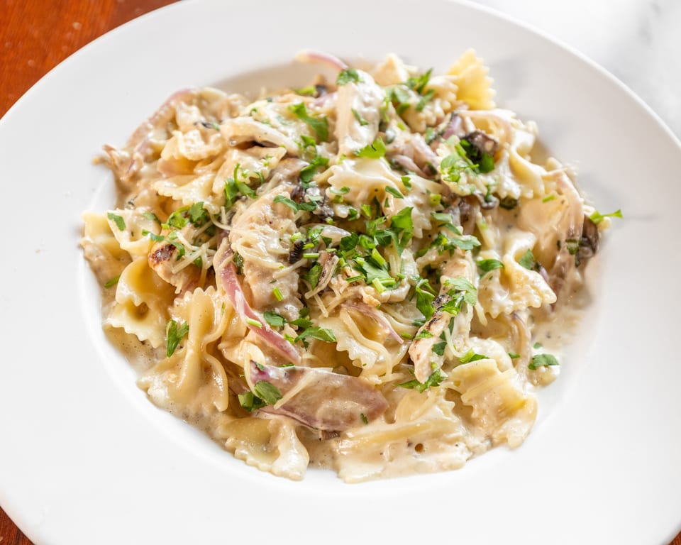 Creamy bowtie pasta with chicken, mushrooms, red onions, and fresh parsley on a white plate.