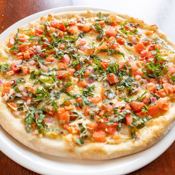 A round bruschetta pizza with diced tomatoes, red onions, and fresh basil on a white plate.