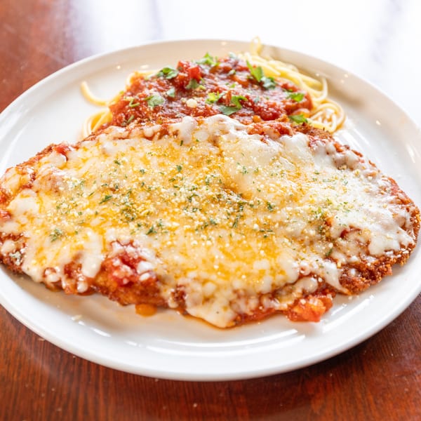 Chicken parmesan with melted cheese, red sauce, and spaghetti on a white plate.