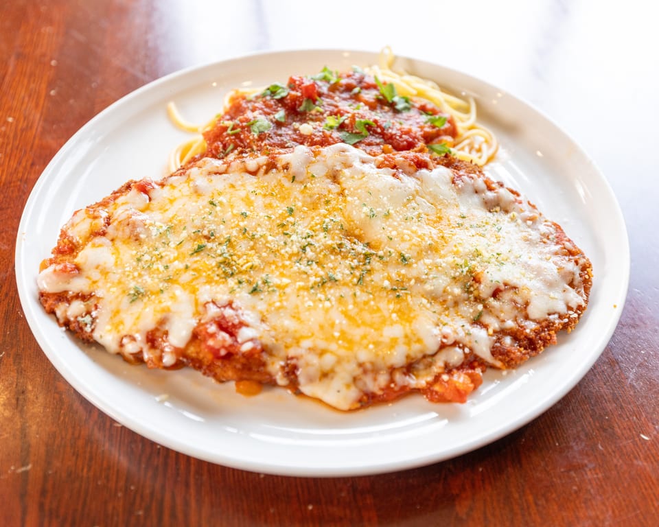 Chicken parmesan with melted cheese, red sauce, and spaghetti on a white plate.
