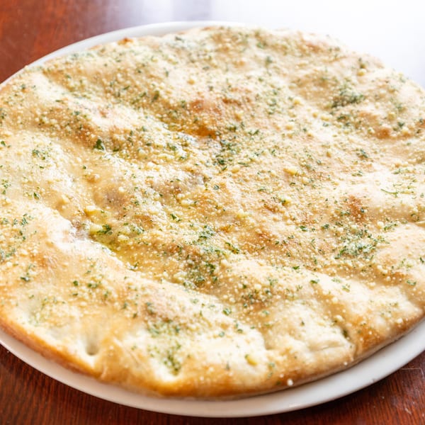 Round garlic bread with melted cheese and green herbs on a white plate.