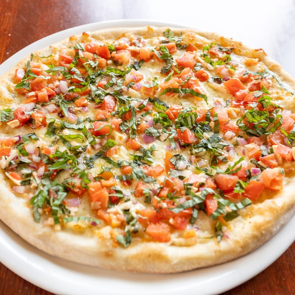 Round pizza with diced tomatoes, red onions, and basil on a white plate.