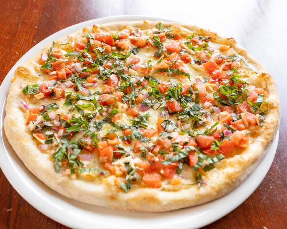 A round pizza with diced tomatoes, red onions, and basil on a white plate.