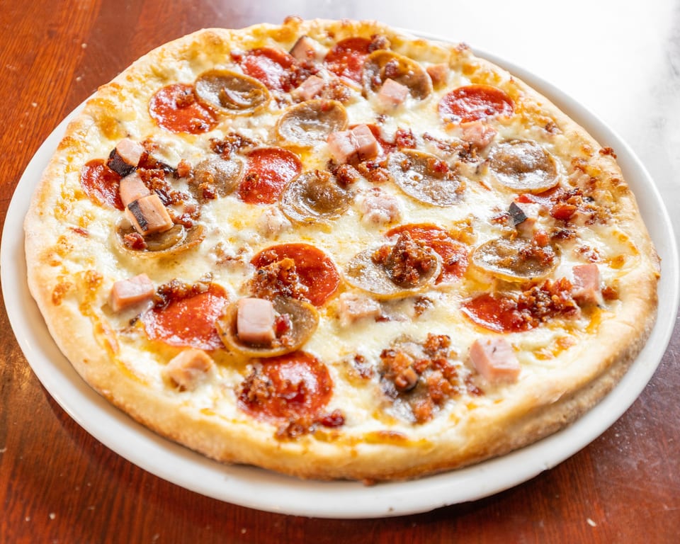 A whole meat lover's pizza with pepperoni, sausage, and ham on a white plate.