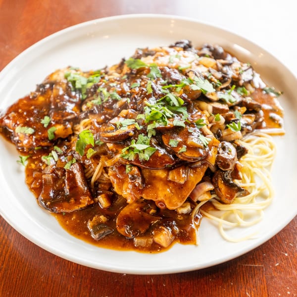 Chicken Marsala with mushrooms, onions, and parsley over spaghetti on a white plate.