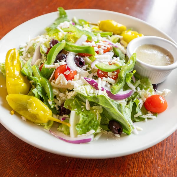 A vibrant Greek salad with lettuce, tomatoes, olives, peppers, onions, feta, and dressing.