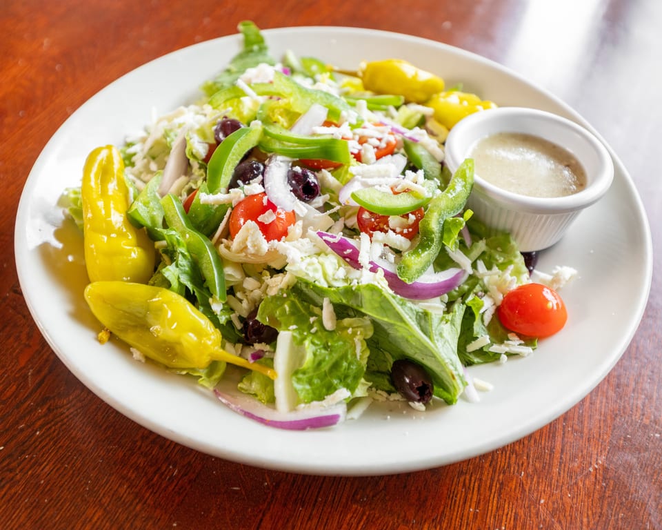 A vibrant Greek salad with lettuce, tomatoes, olives, peppers, onions, feta, and dressing.