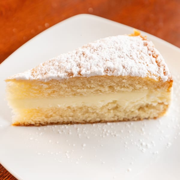 A slice of vanilla cake with a creamy filling and powdered sugar on a white plate.