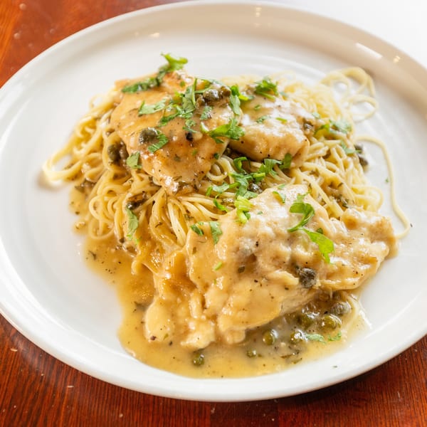 Chicken piccata with capers and parsley over spaghetti on a white plate.