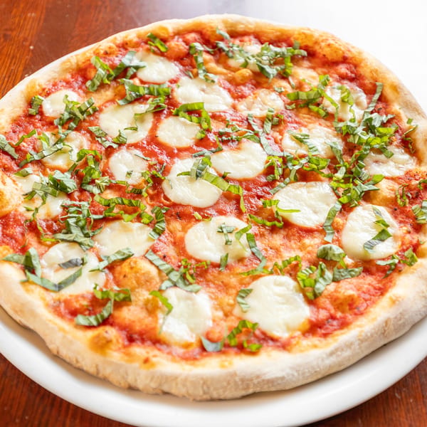 A whole Margherita pizza with fresh mozzarella, tomato sauce, and basil on a white plate.