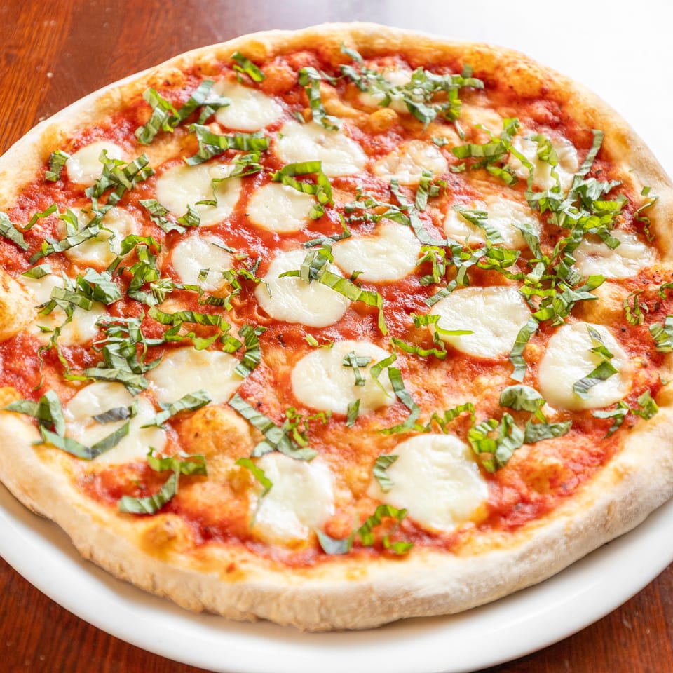 A whole Margherita pizza with fresh mozzarella, tomato sauce, and basil on a white plate.