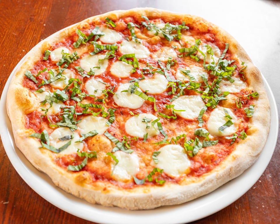 A whole Margherita pizza with fresh mozzarella, tomato sauce, and basil on a white plate.