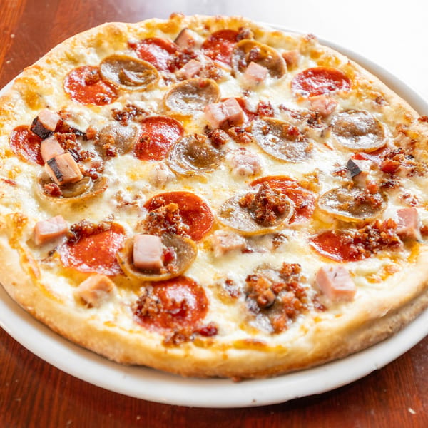 A whole meat lover's pizza with pepperoni, sausage, and ham on a white plate.