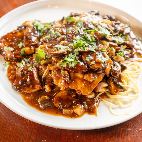 Chicken Marsala with mushrooms, onions, and parsley over spaghetti on a white plate.