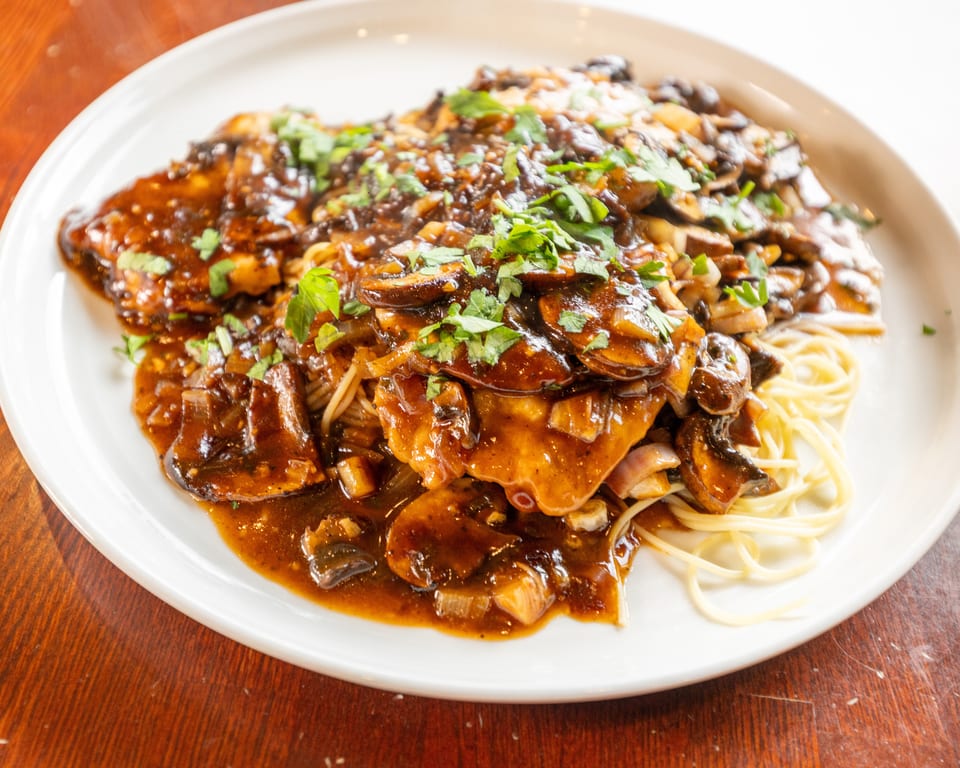 Chicken Marsala with mushrooms and parsley over spaghetti on a white plate.