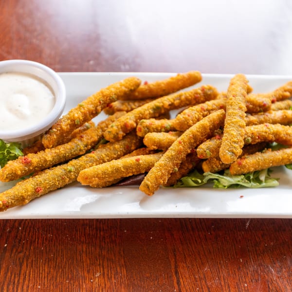 Crispy fried green bean fries with red and green specks, served with ranch dressing on a white plate.