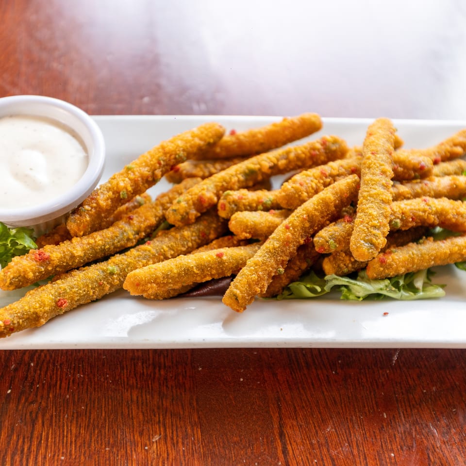 Crispy fried green bean fries with red and green specks, served with ranch dressing on a white plate.