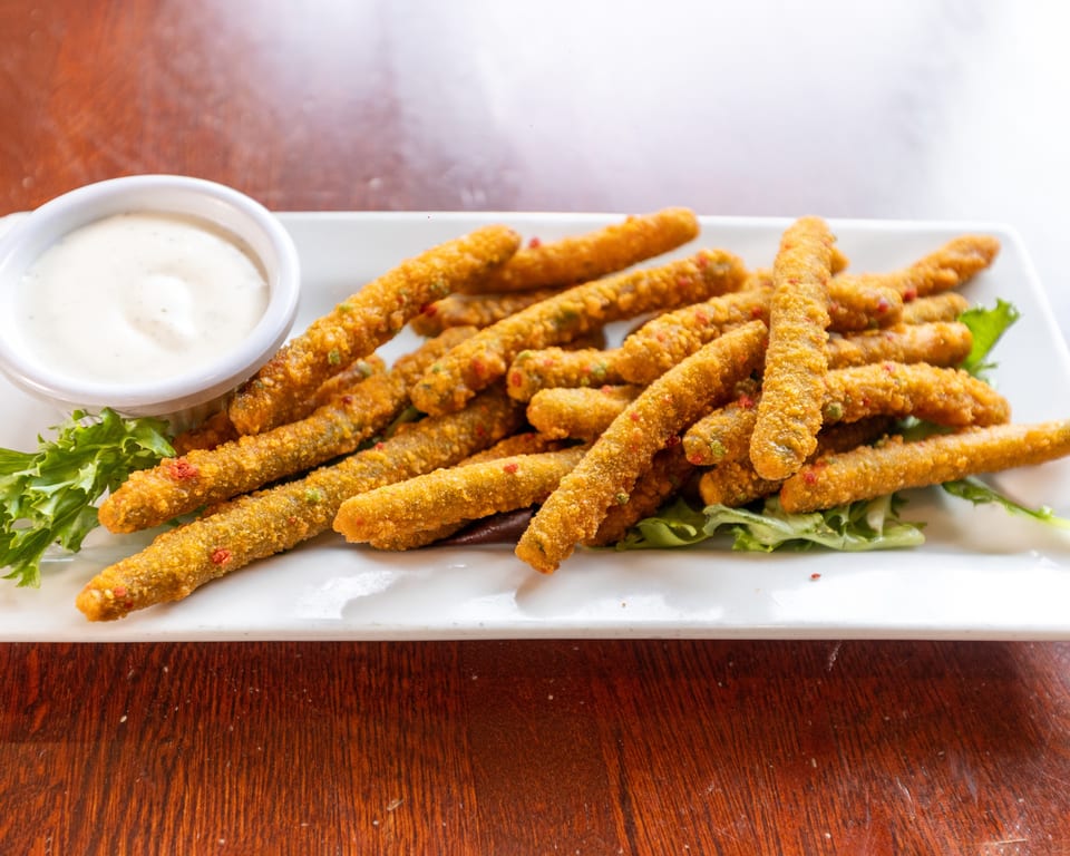 Crispy fried green bean fries with red and green specks, served with a side of ranch dressing.