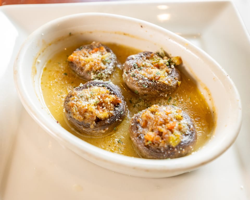 Four stuffed mushrooms with cheese and herbs in a buttery sauce, served in a white oval dish.