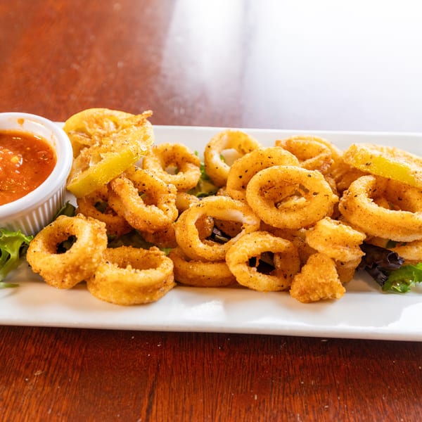 Crispy fried calamari rings with lemon wedges and a side of red marinara sauce on a white plate.