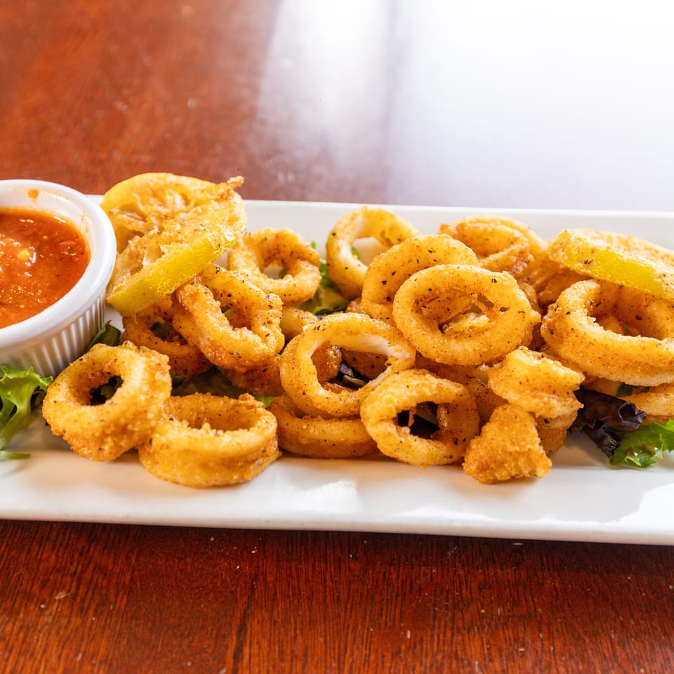 Crispy fried calamari rings with lemon wedges and a side of red marinara sauce on a white plate.