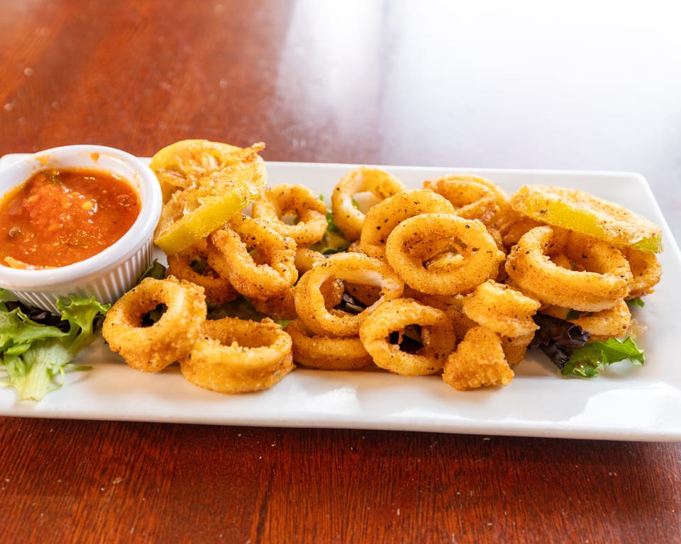 Crispy fried calamari rings with lemon wedges, fresh greens, and a side of marinara sauce.