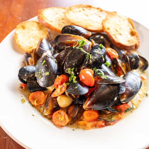 Steamed mussels in a white wine sauce with cherry tomatoes, garlic, and toasted bread.