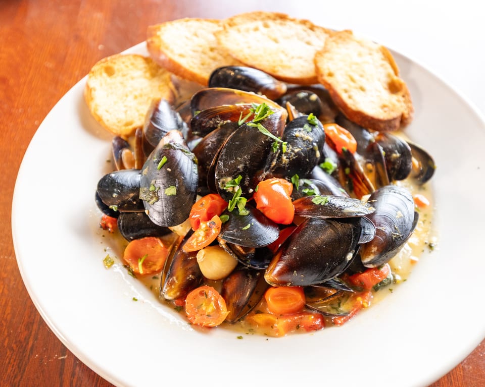 Steamed mussels in a white wine sauce with cherry tomatoes, garlic, and toasted bread.