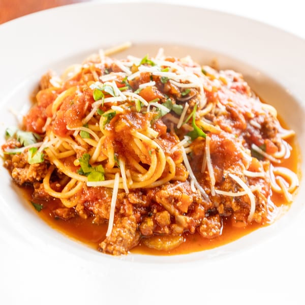 Spaghetti with meat sauce, parmesan cheese, and fresh herbs in a white bowl.