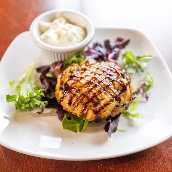 Golden-brown crab cake drizzled with balsamic glaze, served with mixed greens and tartar sauce.