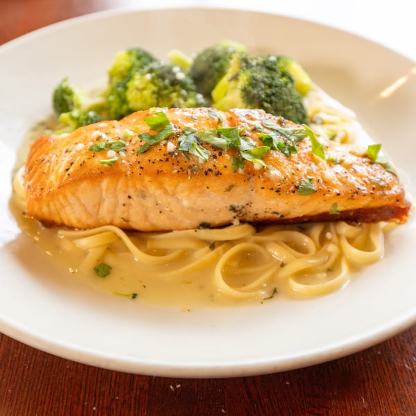 Pan-seared salmon with fresh parsley, linguine pasta in cream sauce, and steamed broccoli on a white plate.