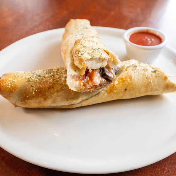 Two golden-brown calzones, one cut open to reveal melted cheese and mushrooms, with a side of marinara.