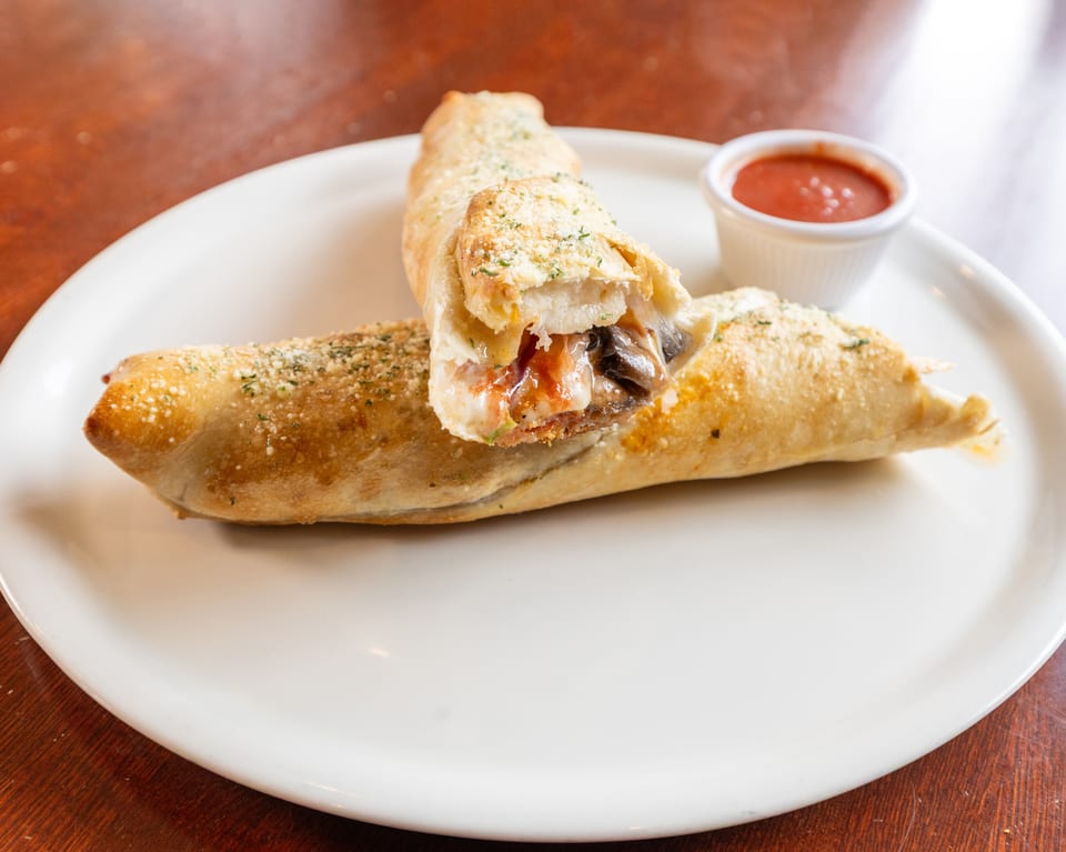 Two golden-brown calzones, one cut open to reveal melted cheese and mushrooms, with a side of marinara.