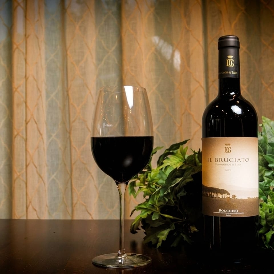 A glass of red wine and a bottle of Il Bruciato Bolgheri wine on a dark table.